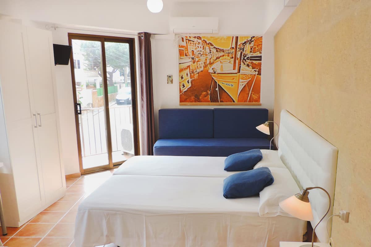 A hotel room with a bed, a blue sofa, a painting, and a view through the door.