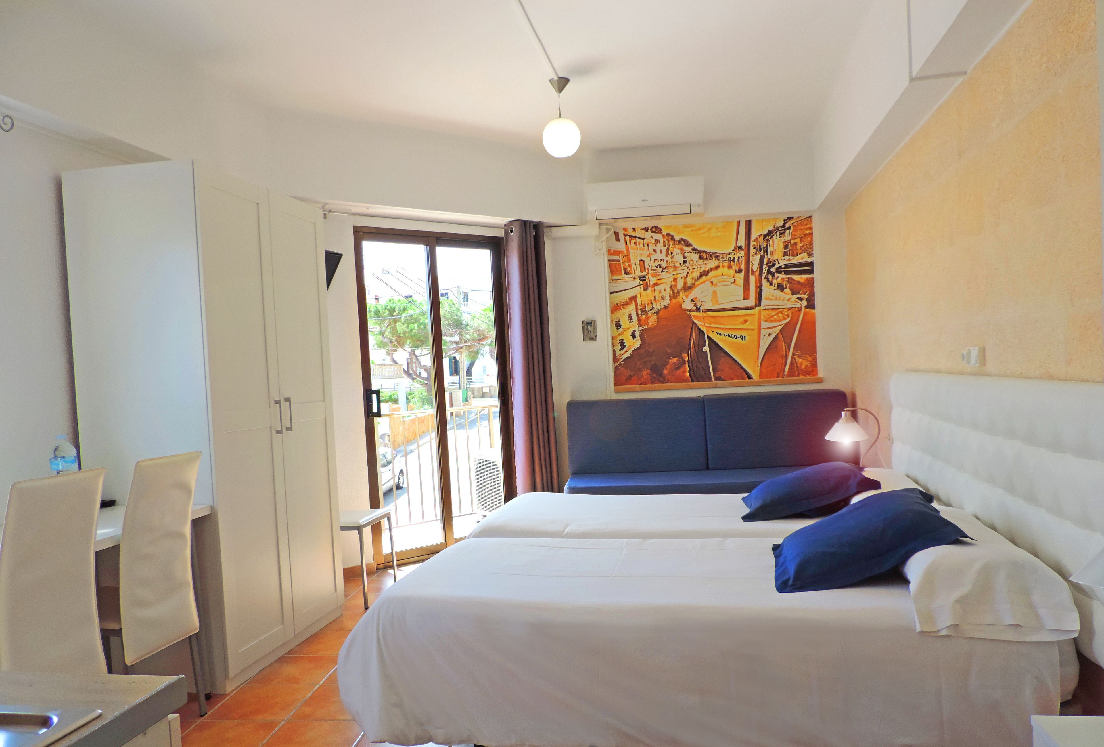 A hotel room with a bed, a desk, and a chair. There is a painting on the wall and a window with curtains.