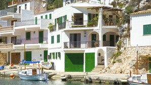 Un bâtiment situé sur la côte, doté de nombreux balcons, de volets verts et d’un quai où sont amarrés des bateaux.