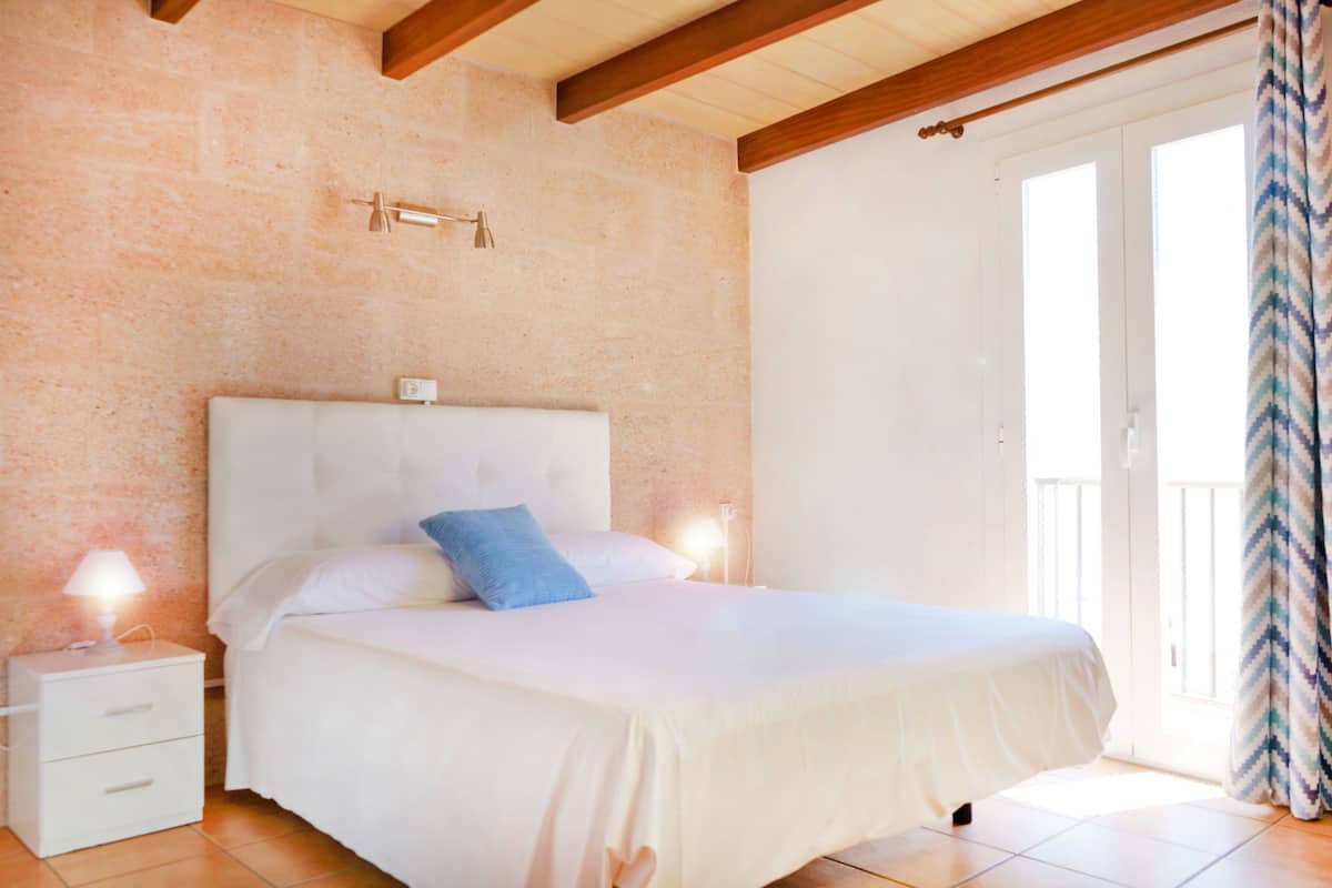 A bedroom with a bed, nightstands, a wall-mounted light, and a sliding glass door.