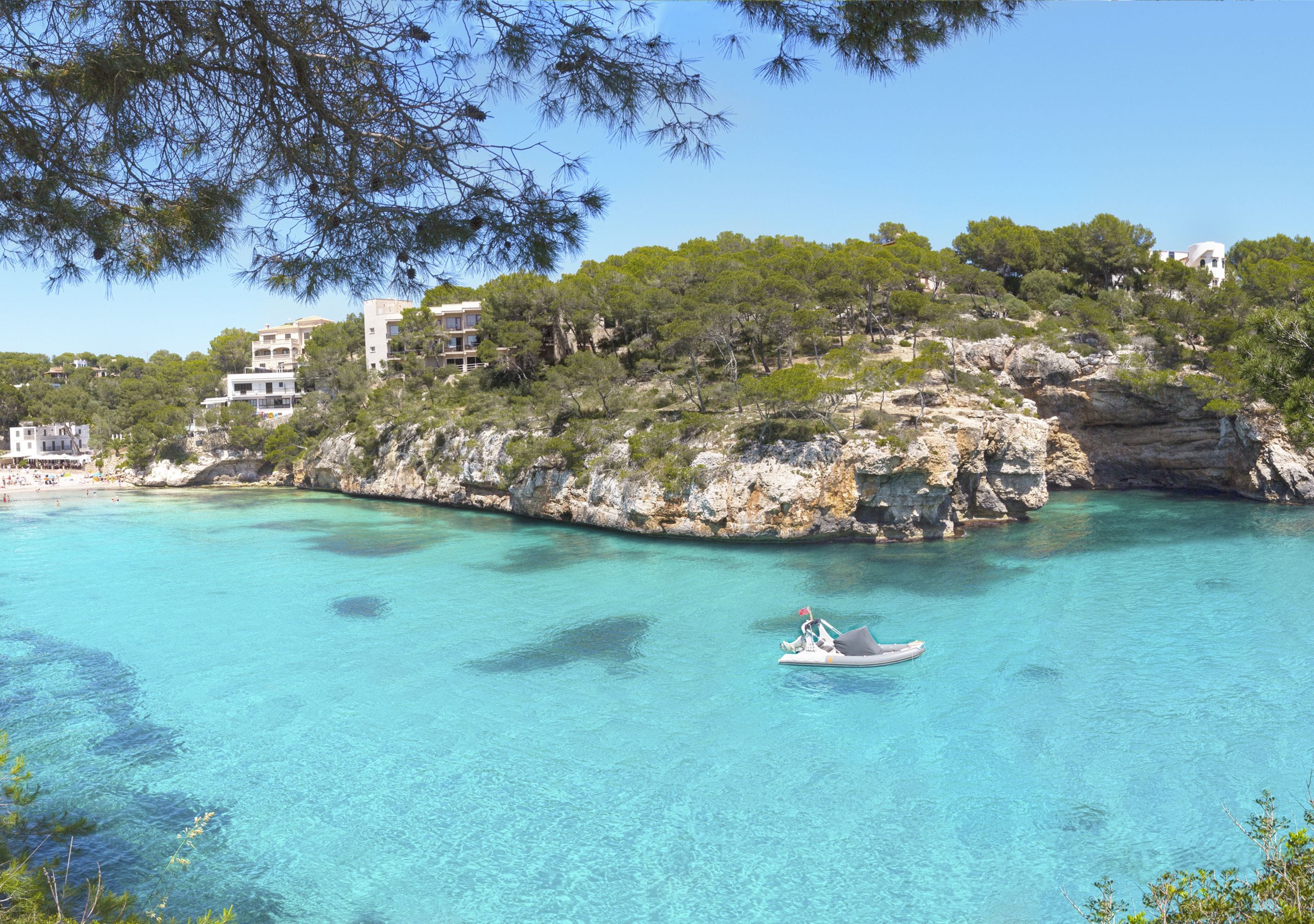 A coastal area with clear turquoise waters, a rocky cliff with buildings, and a small boat.
