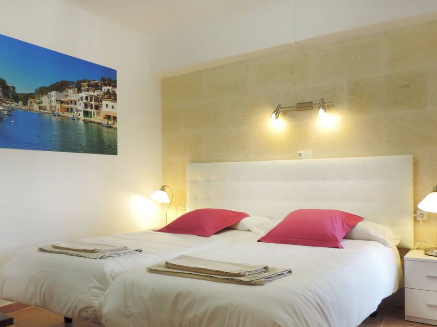 Ein Hotelzimmer mit einem Bett, zwei Nachttischlampen, einem Nachttisch, einem Sessel und einem Wandbild einer Küstenstadt.