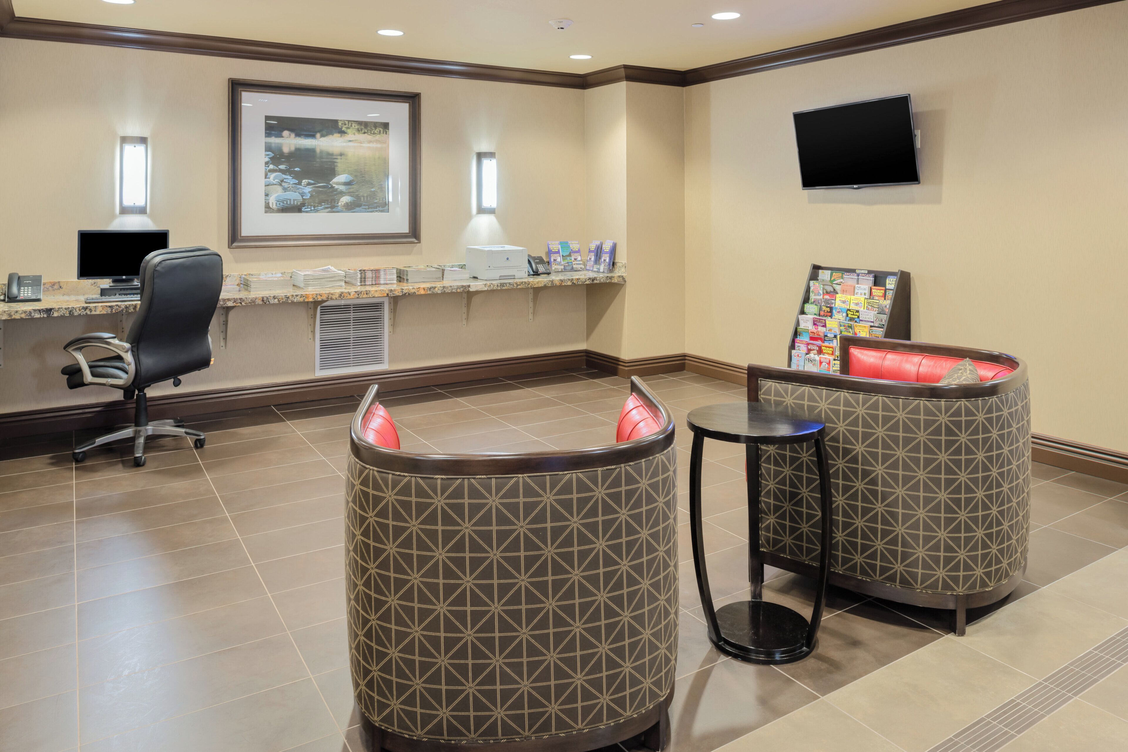 A reception area with a desk, computer, phone, framed artwork, magazines, and two patterned chairs.
