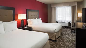 A hotel room with two beds, a desk, a TV, and a window with curtains.