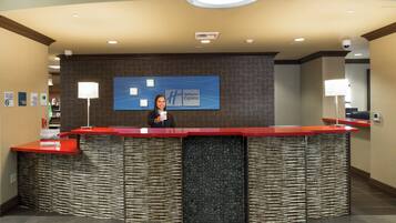 A reception desk with a modern design, a large blue sign above it, and a woman standing behind the desk.