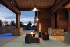 An outdoor patio area with stone walls, wicker furniture, and a central fire feature. - Holiday Inn Express Klamath - Redwood Ntl Pk Area by IHG (Klamath)