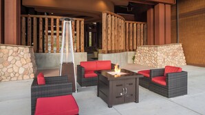 An outdoor seating area with wicker furniture and red cushions, a fire feature, and a stone wall. - Holiday Inn Express Klamath - Redwood Ntl Pk Area by IHG (Klamath)