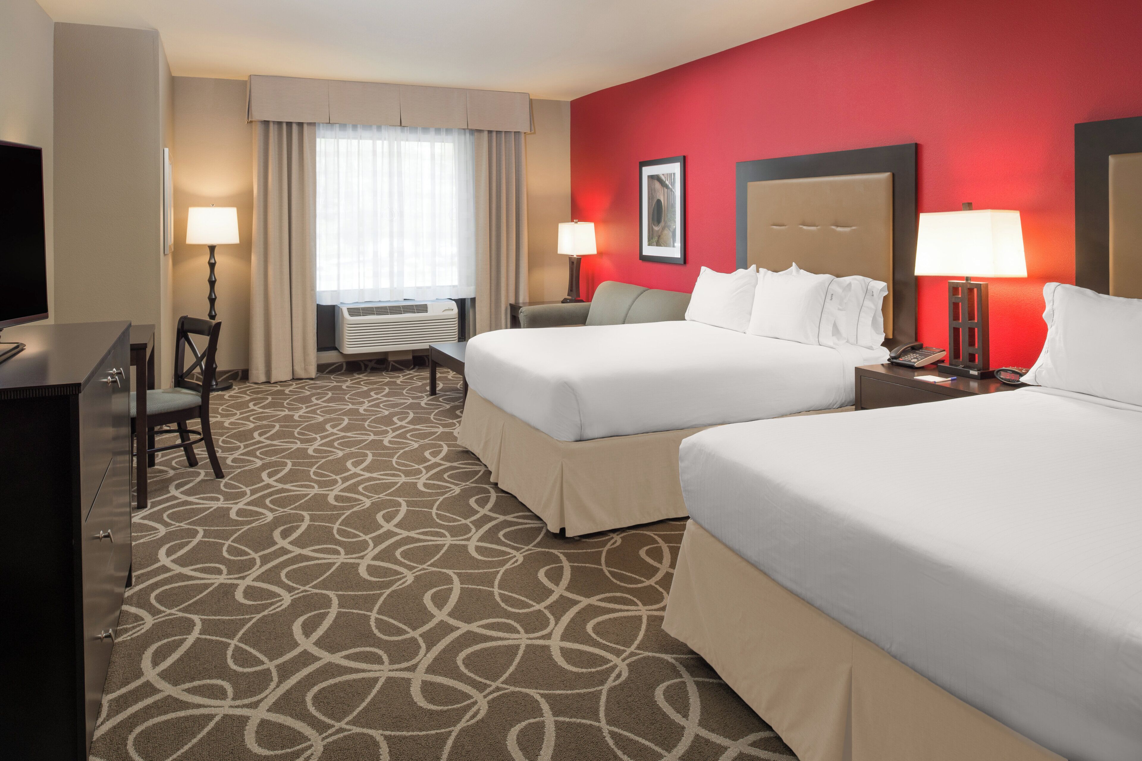A hotel room with two beds, a desk, a chair, a TV, and a window with curtains.