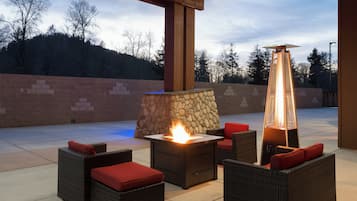 An outdoor patio with a stone fireplace, a table with a fire, and wicker furniture with red cushions.
