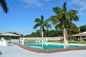 A swimming pool with lounge chairs, palm trees, and a building with a tiled roof. - Pousada Ohana (Búzios)