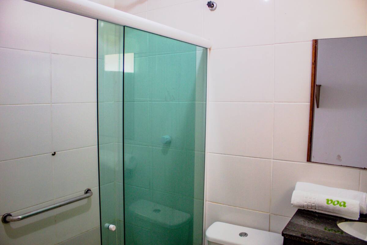 A bathroom with a glass shower enclosure, a white toilet, and a towel with "boa" on it.