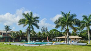 Una zona de piscina con palmeras, un edificio pequeño y un coche.