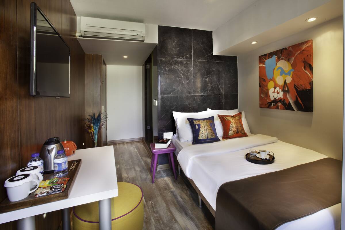 Habitación de hotel moderna con cama, escritorio y bandeja con alimentos para el desayuno, televisión y un cuadro abstracto grande en la pared.
