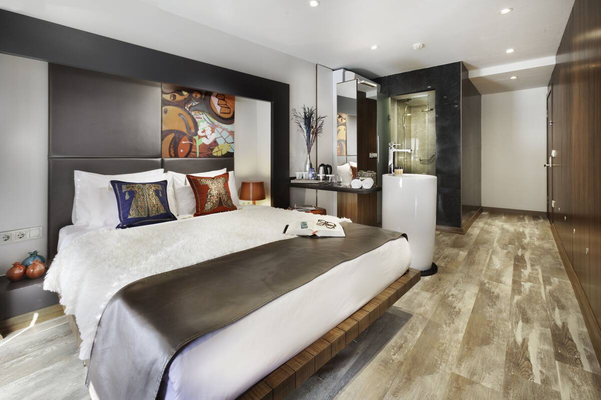 Un dormitorio moderno con una cama grande, una mesita de noche, un espejo y un baño con ducha y lavabo.