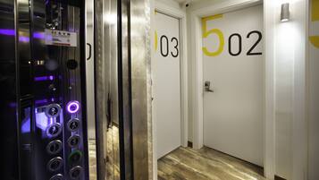 Um elevador com painel de controle e um corredor com portas numeradas 103 e 502.