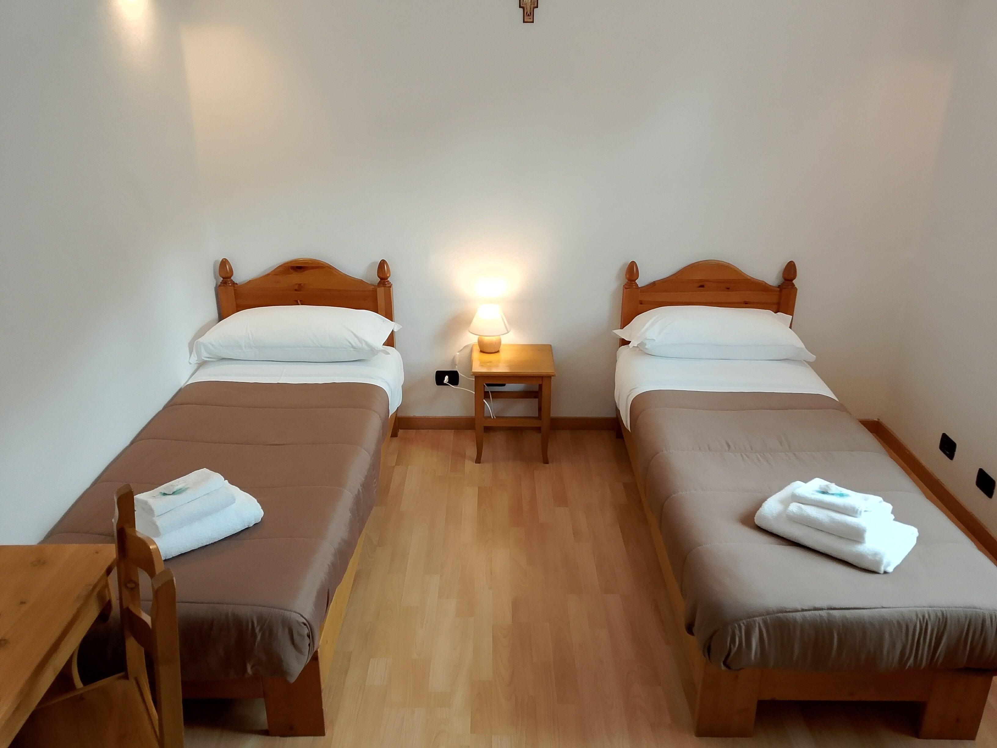 Ein Zimmer mit zwei Betten, jeweils mit einem hölzernen Kopfteil, einem Nachttisch mit Lampe und einem Holzstuhl.