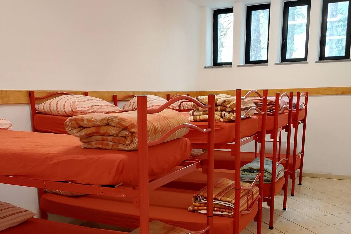 Bunk beds with orange bedding, a tiled floor, and windows with views of trees.
