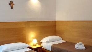 A hotel room with two single beds, a wooden headboard, a wall-mounted cross, and a nightstand with a lamp.