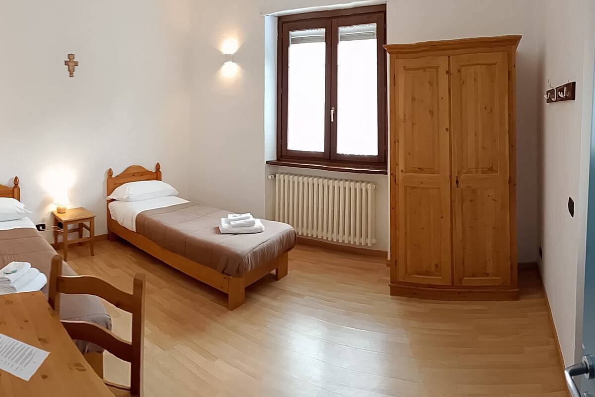 A bedroom with a bed, a wooden wardrobe, a window, and a desk with a chair.