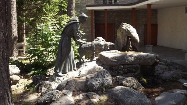 A statue of a figure with a dog in a naturalistic setting with rocks and trees.