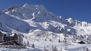 A snow-covered mountain resort with a large building featuring multiple balconies and a ski lift in the background. - Hotel Piandineve (Ponte di Legno)