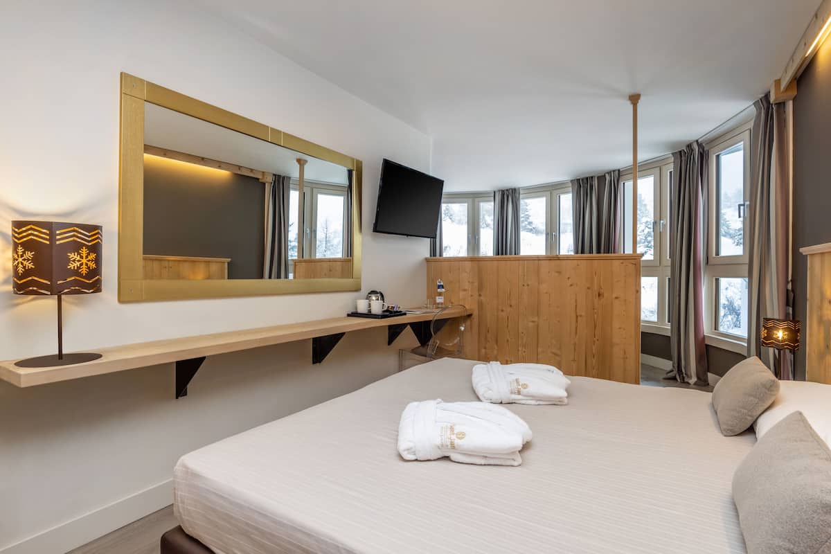 A hotel room with a large bed, a wooden dresser, a mirror, a television, and a window with curtains.