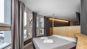 A modern hotel room with a large bed, wooden headboard, and a TV mounted on the wall. - Hotel Piandineve (Ponte di Legno)