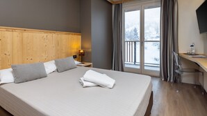 A hotel room with a large bed, wooden headboard, a desk with a chair, a TV, and a window with curtains. - Hotel Piandineve (Ponte di Legno)