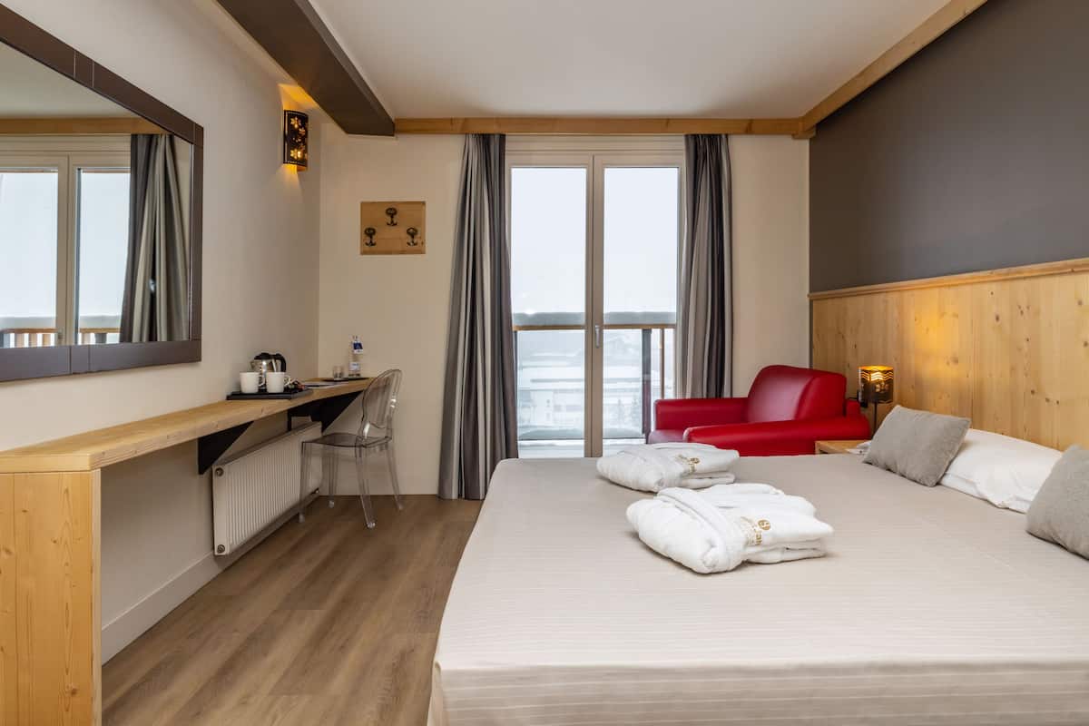 A hotel room with a bed, a desk, a chair, a red sofa, and a view of the sea.
