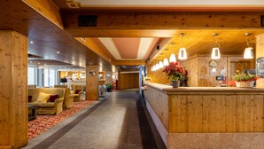 A hotel lobby with wooden paneling, a reception desk, seating area, and a bar. - Hotel Piandineve (Ponte di Legno)