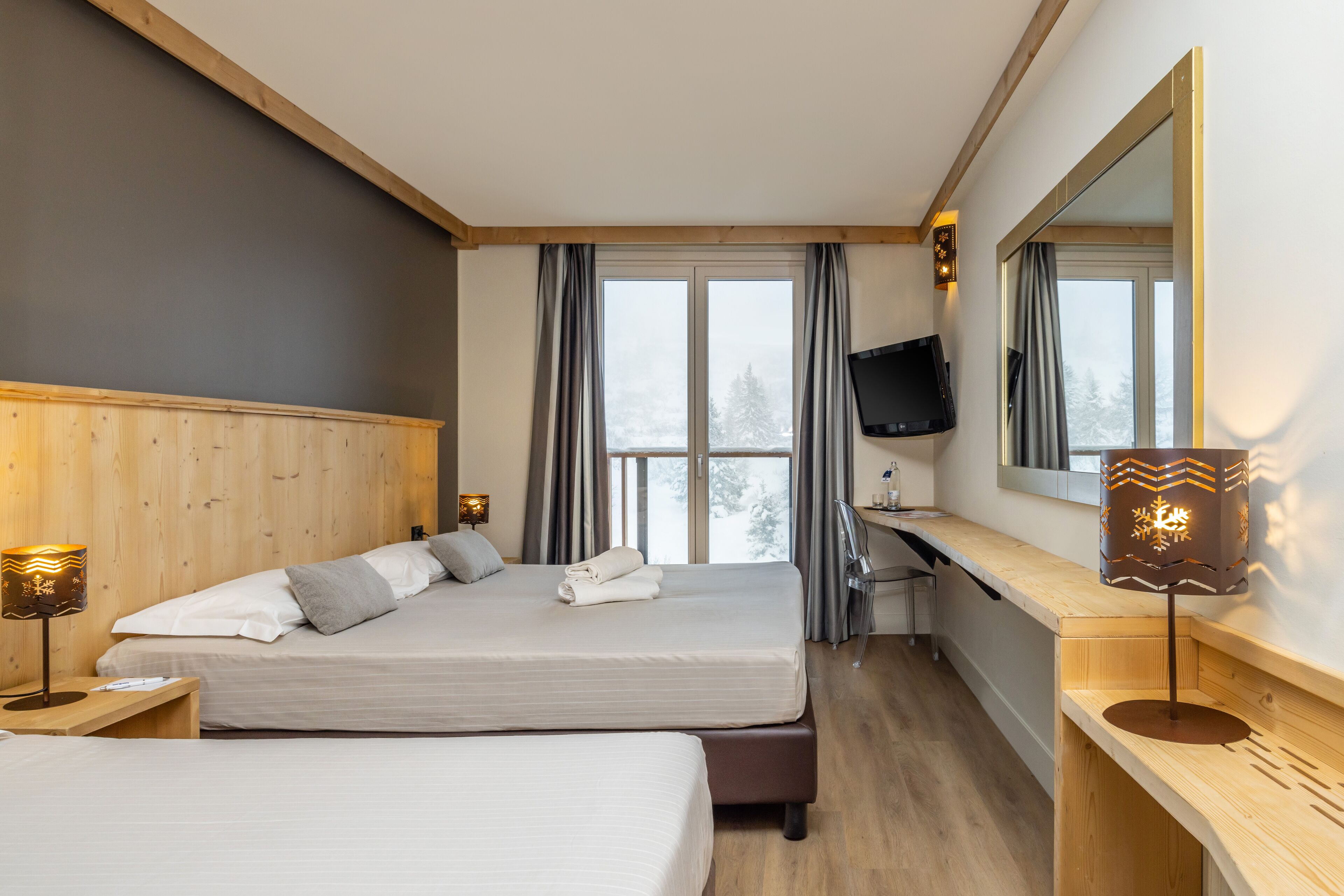 Une chambre d’hôtel avec deux lits, une télévision, un bureau et une fenêtre avec des rideaux.