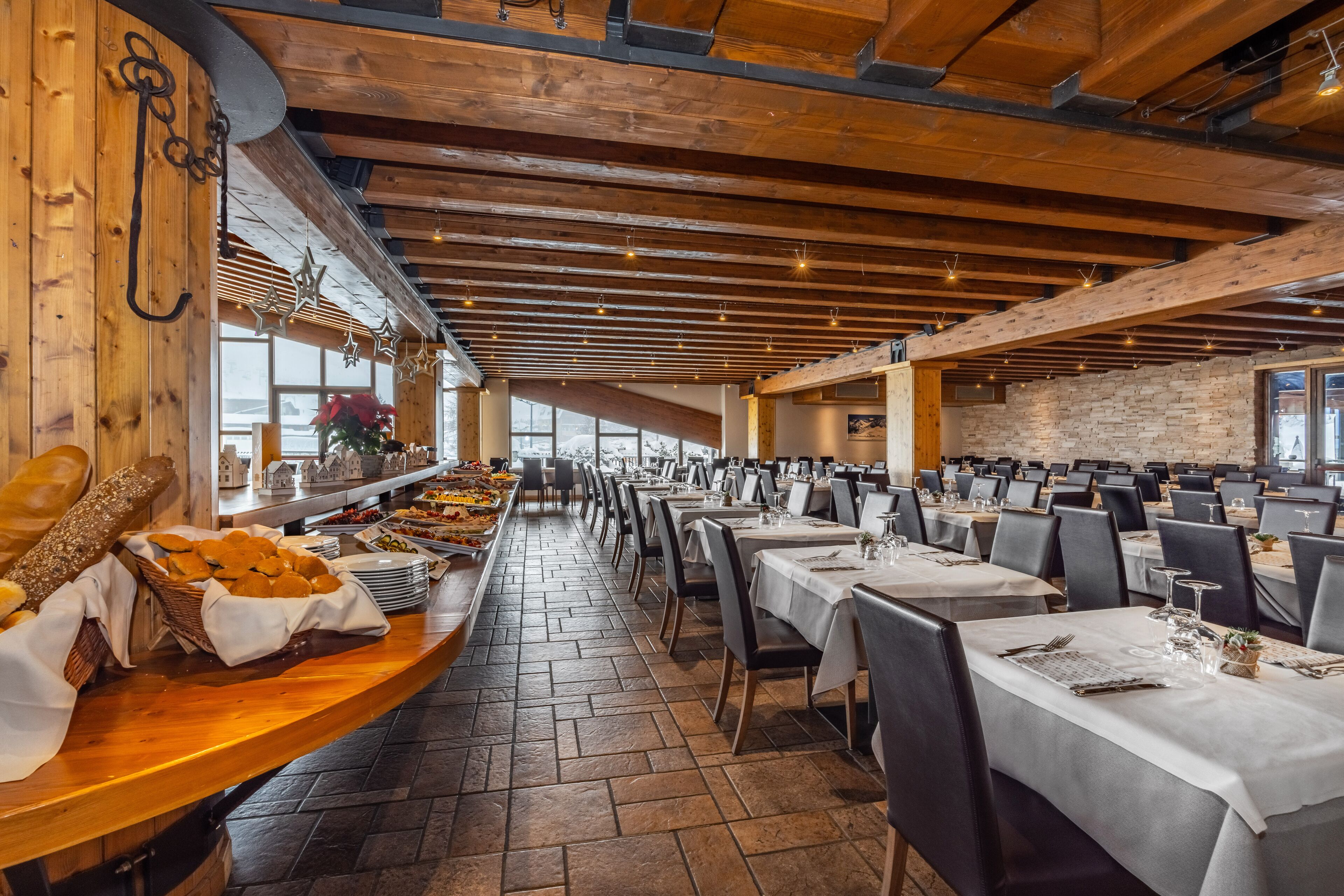A spacious dining hall with high wooden ceilings and brick walls, featuring long tables set for dining.