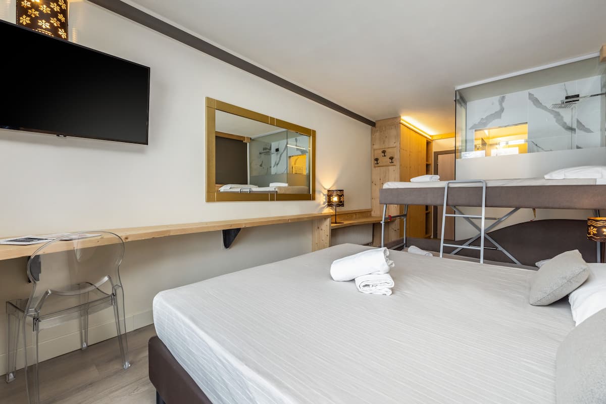 A hotel room with a bed, a desk with a chair, a television, a mirror, and a bathroom with a shower and sink.