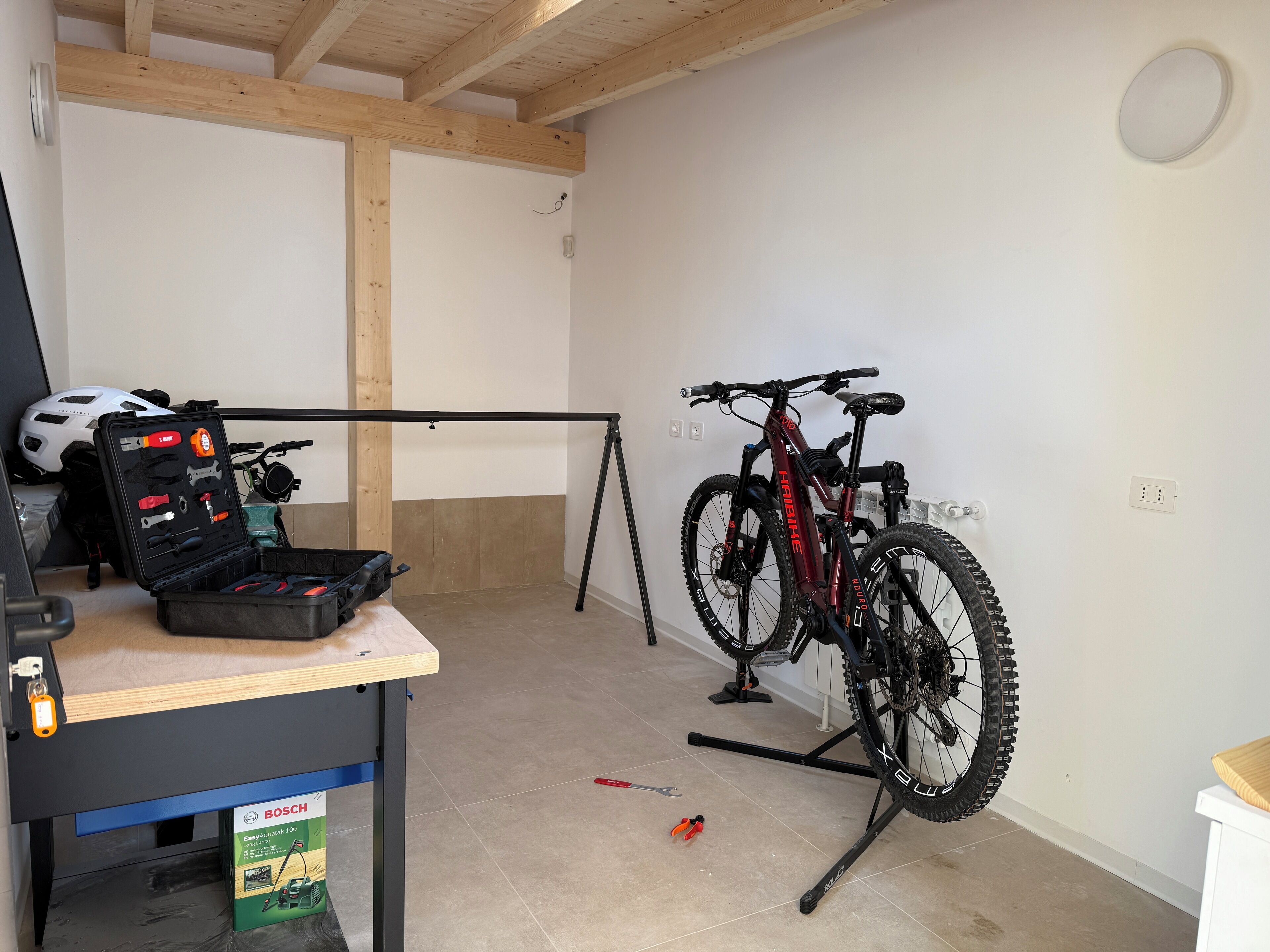 A room with a bicycle mounted on a stand, a toolbox with tools, and a helmet on the floor.