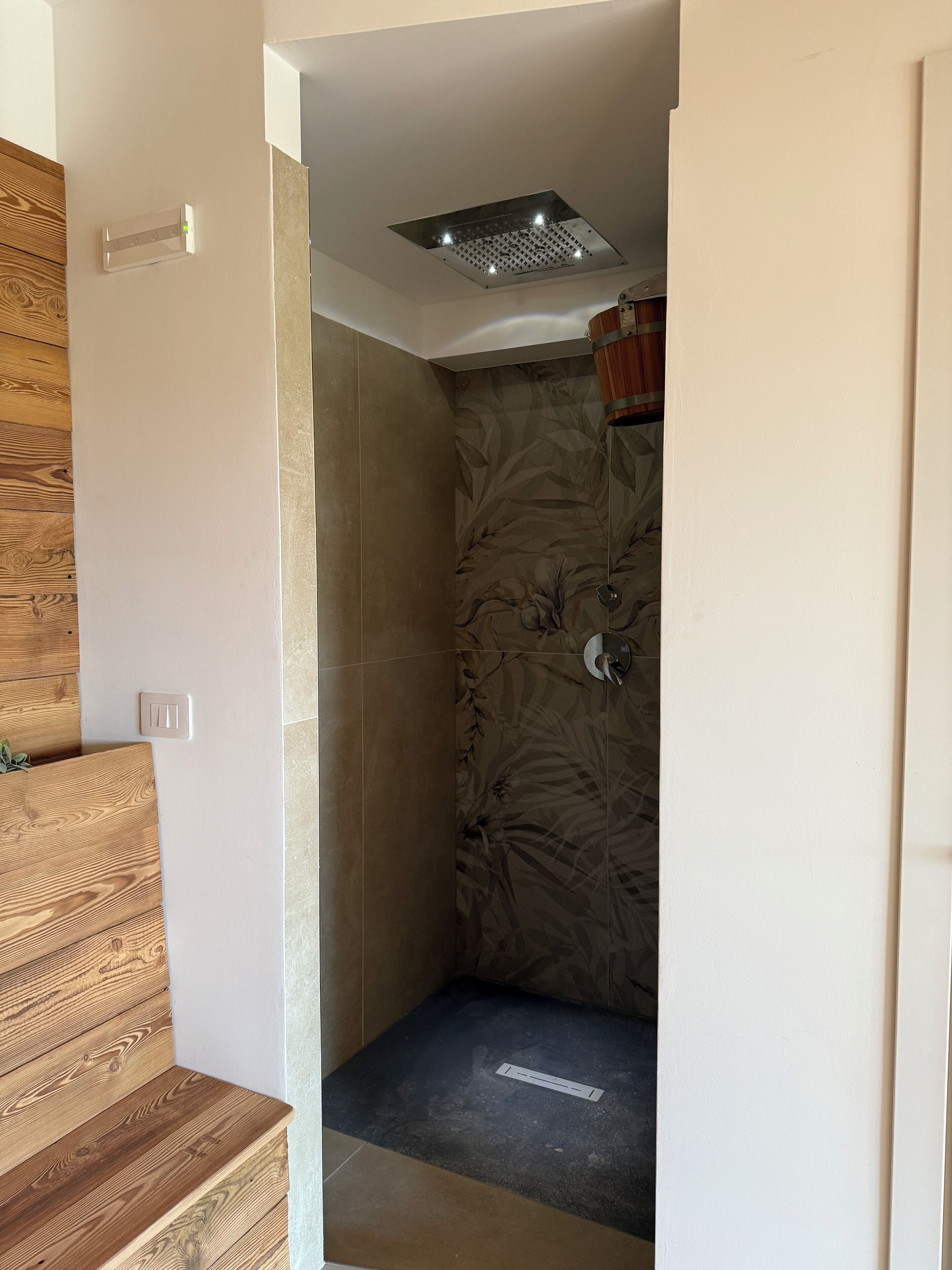 Una ducha con un revestimiento de pared estampado con motivos florales, una luz en el techo y un banco de madera.