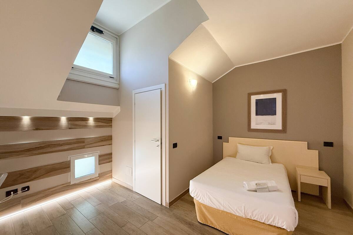 A modern bedroom with a skylight, a bed with a headboard, a bedside table, and a framed picture on the wall.
