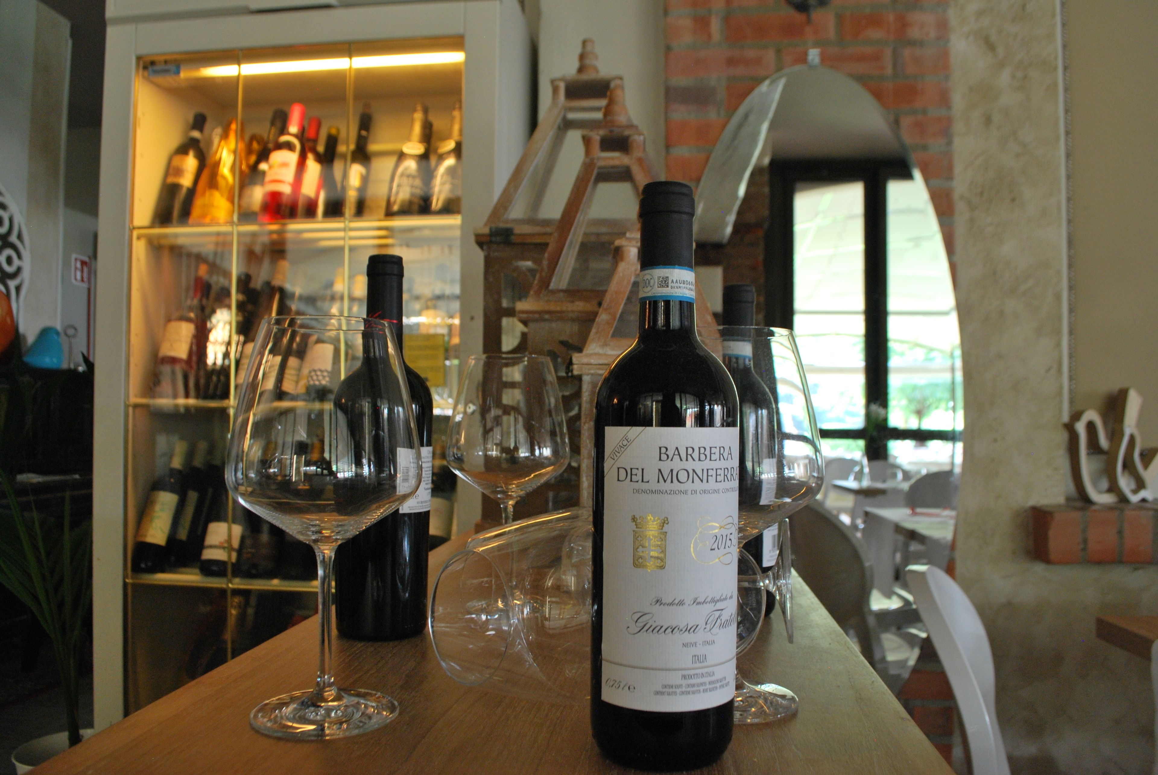 Una botella de vino sobre una mesa de madera con varios vasos de vino vacíos. Se ve una botellera con botellas al fondo.