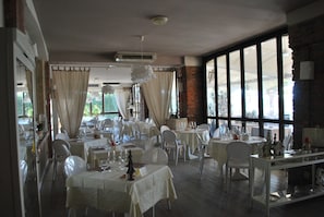 Comedor con mesas dispuestas para una comida, ventanas amplias y una pared de ladrillo.