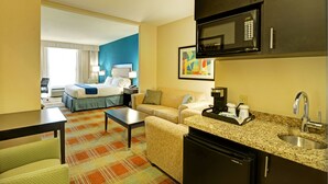 A hotel room with a bed, a sofa, a coffee table, a kitchenette with a microwave, and a sink.