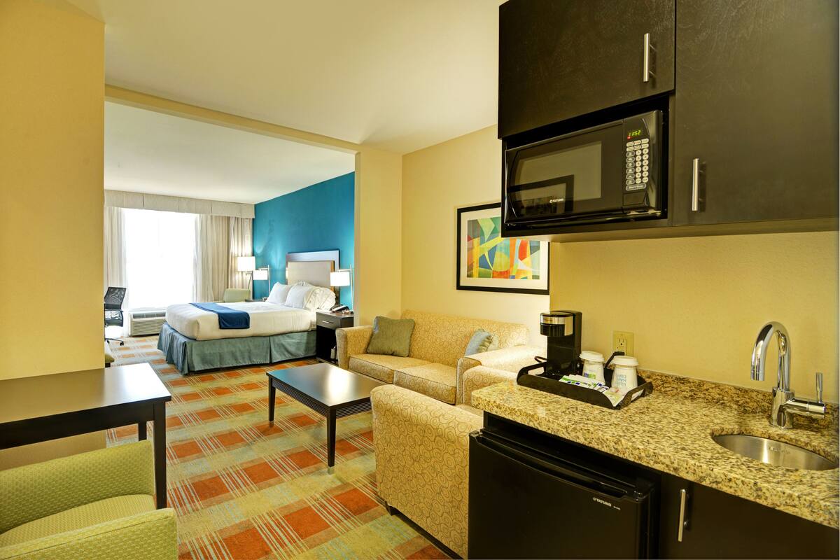 A hotel room with a bed, a sofa, a coffee table, a kitchenette with a microwave, and a sink.