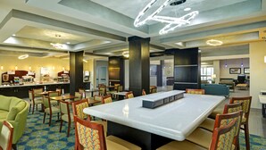 A hotel lobby with a central island table, multiple seating areas, and a bar.