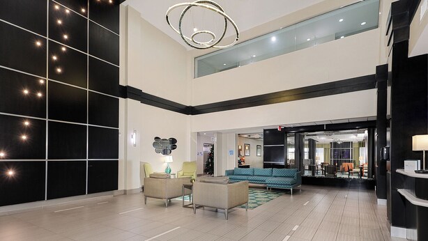 A spacious lobby with a high ceiling, a modern chandelier, and a seating area with sofas and armchairs.