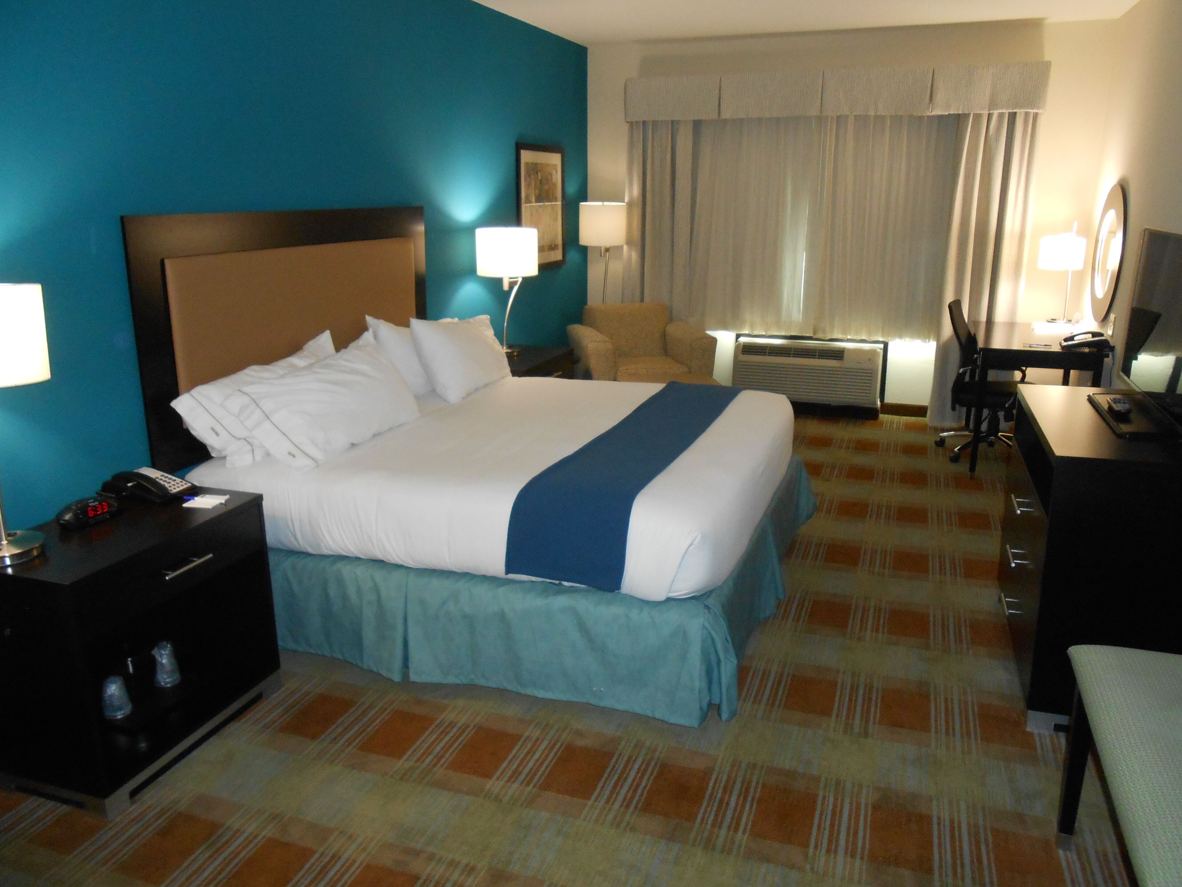 A hotel room with a large bed, bedside tables, a desk, a chair, and a desk lamp.