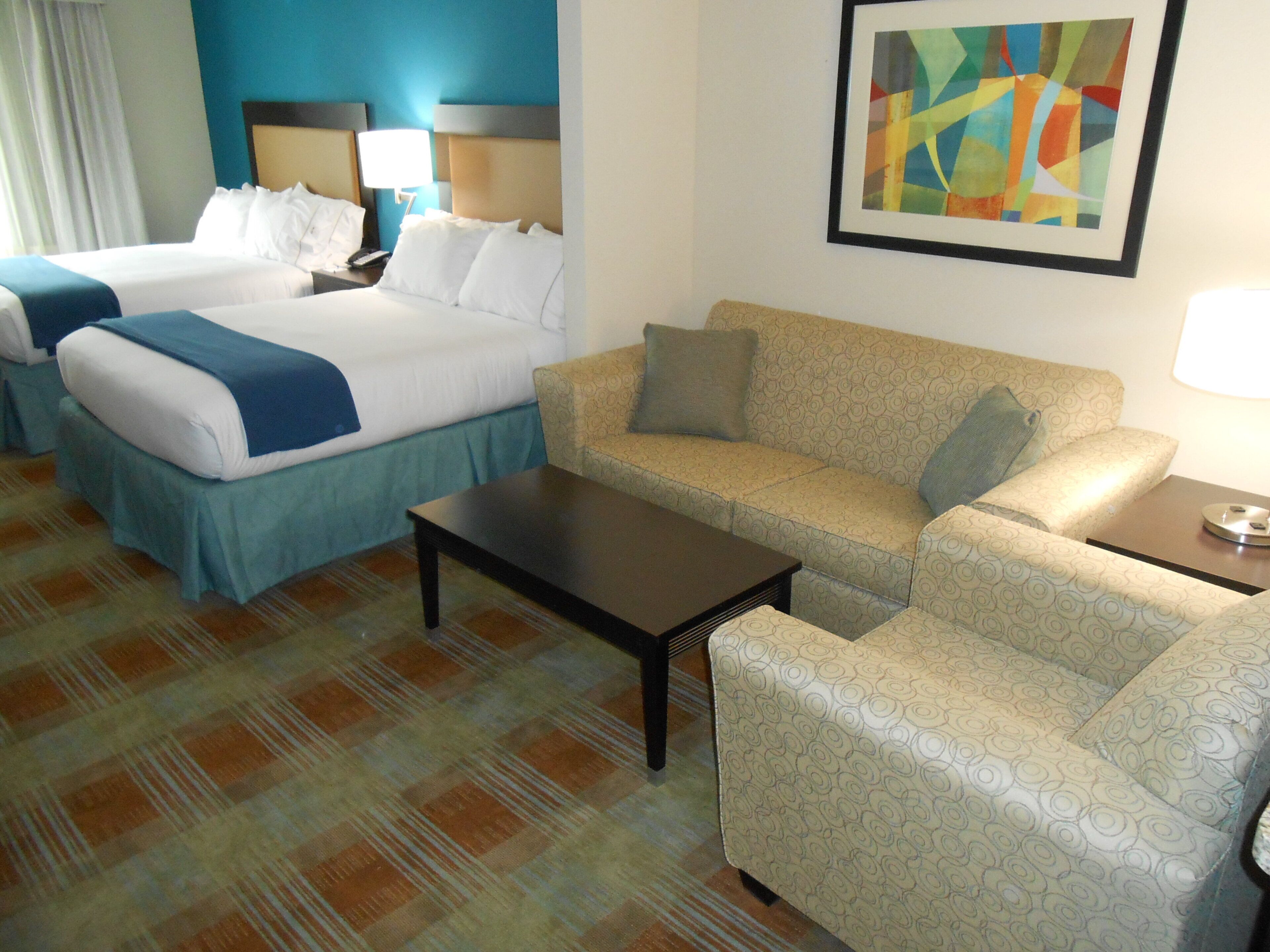 Habitación de hotel con dos camas, un sofá, una mesa de centro y un cuadro en la pared.