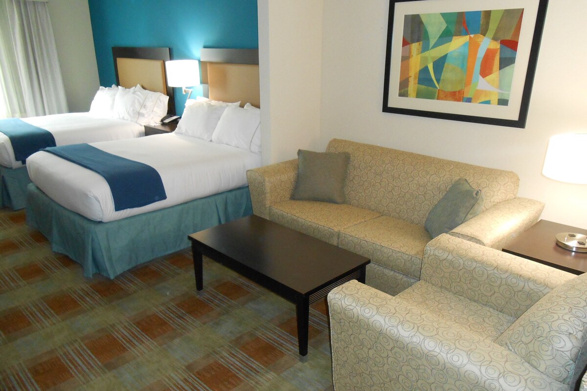 A hotel room with two beds, a sofa, a coffee table, and a painting on the wall.
