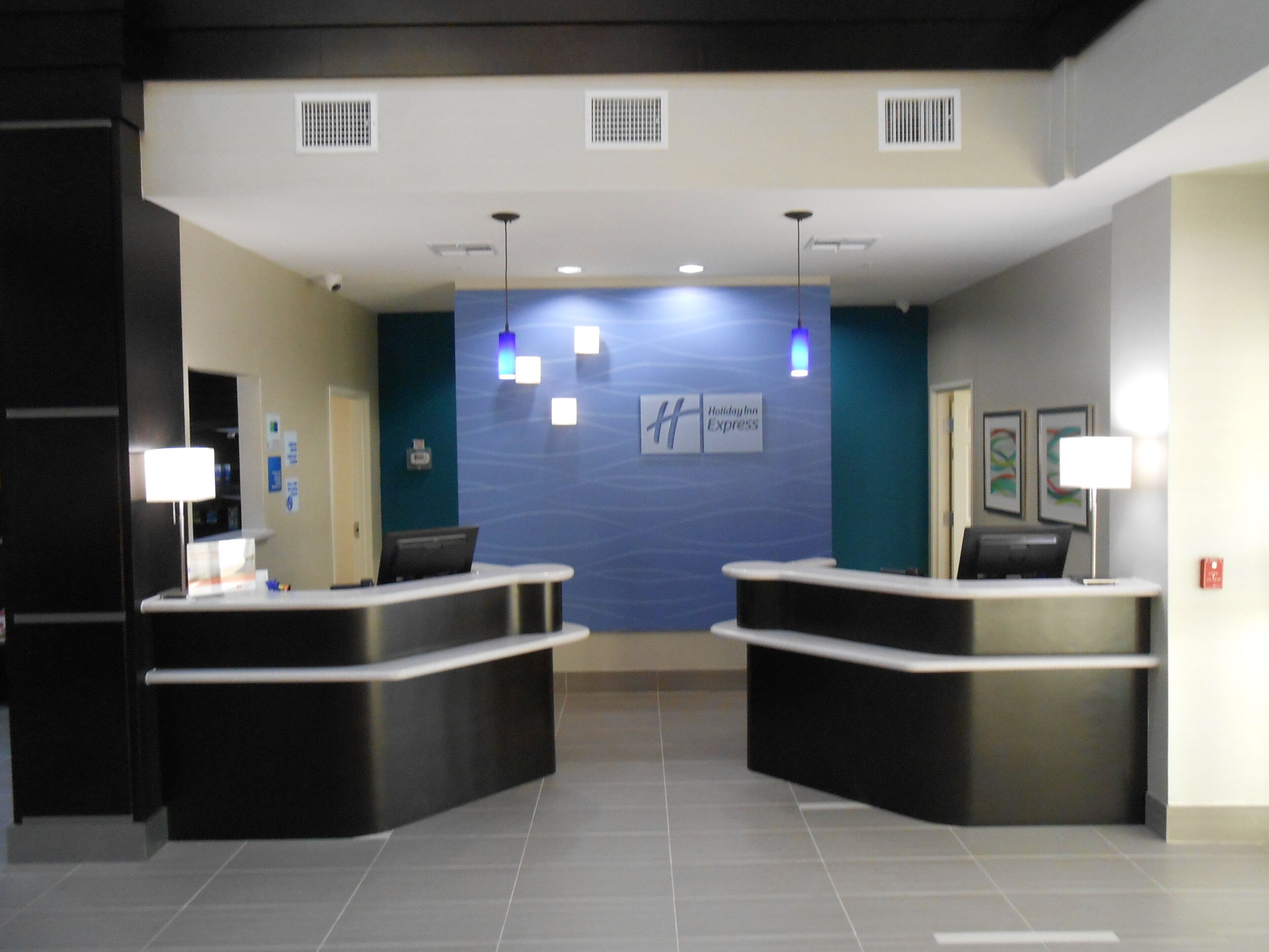 A hotel reception area with two reception desks, a blue accent wall, and a sign for Holiday Inn Express.