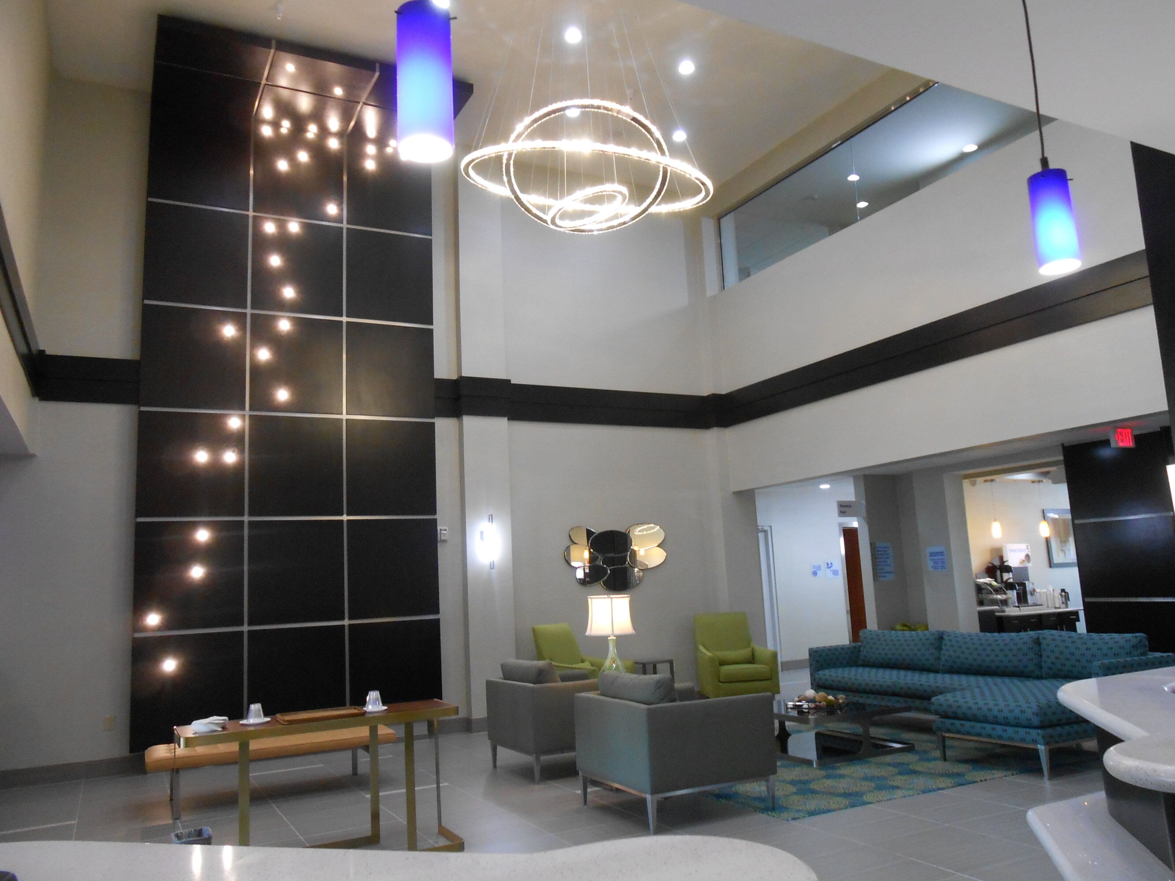 Un hall d’entrée moderne avec un plafond haut, un espace détente avec un banc et des fauteuils, et un canapé bleu.