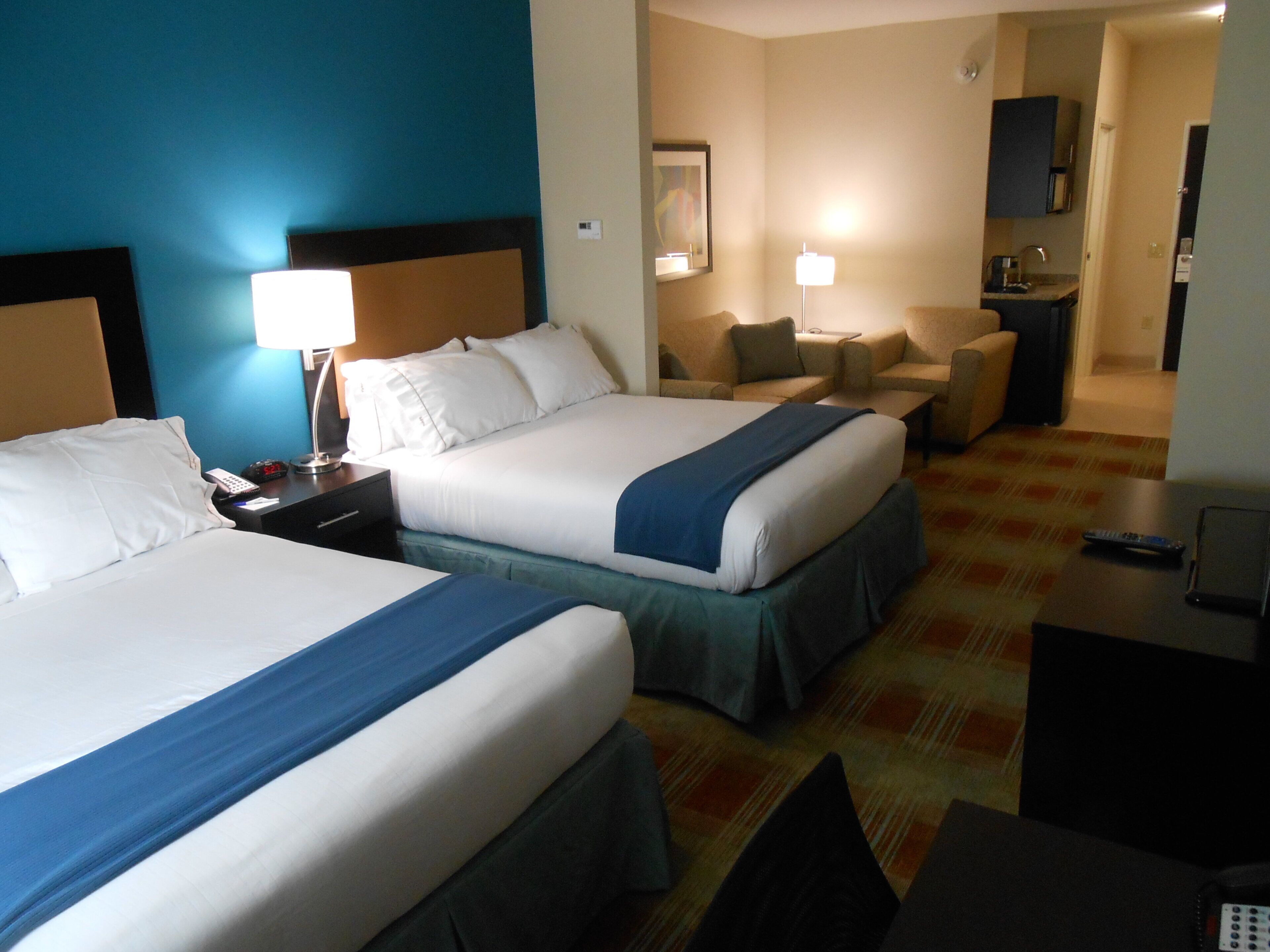 Habitació d'hotel amb dos llits, un escriptori, una cadira i una cuineta petita.