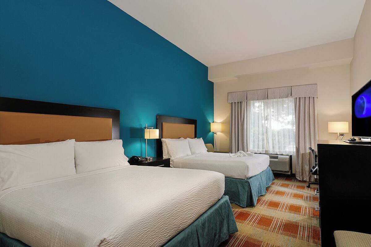 A hotel room with two beds, a television, a desk, and a window with curtains.