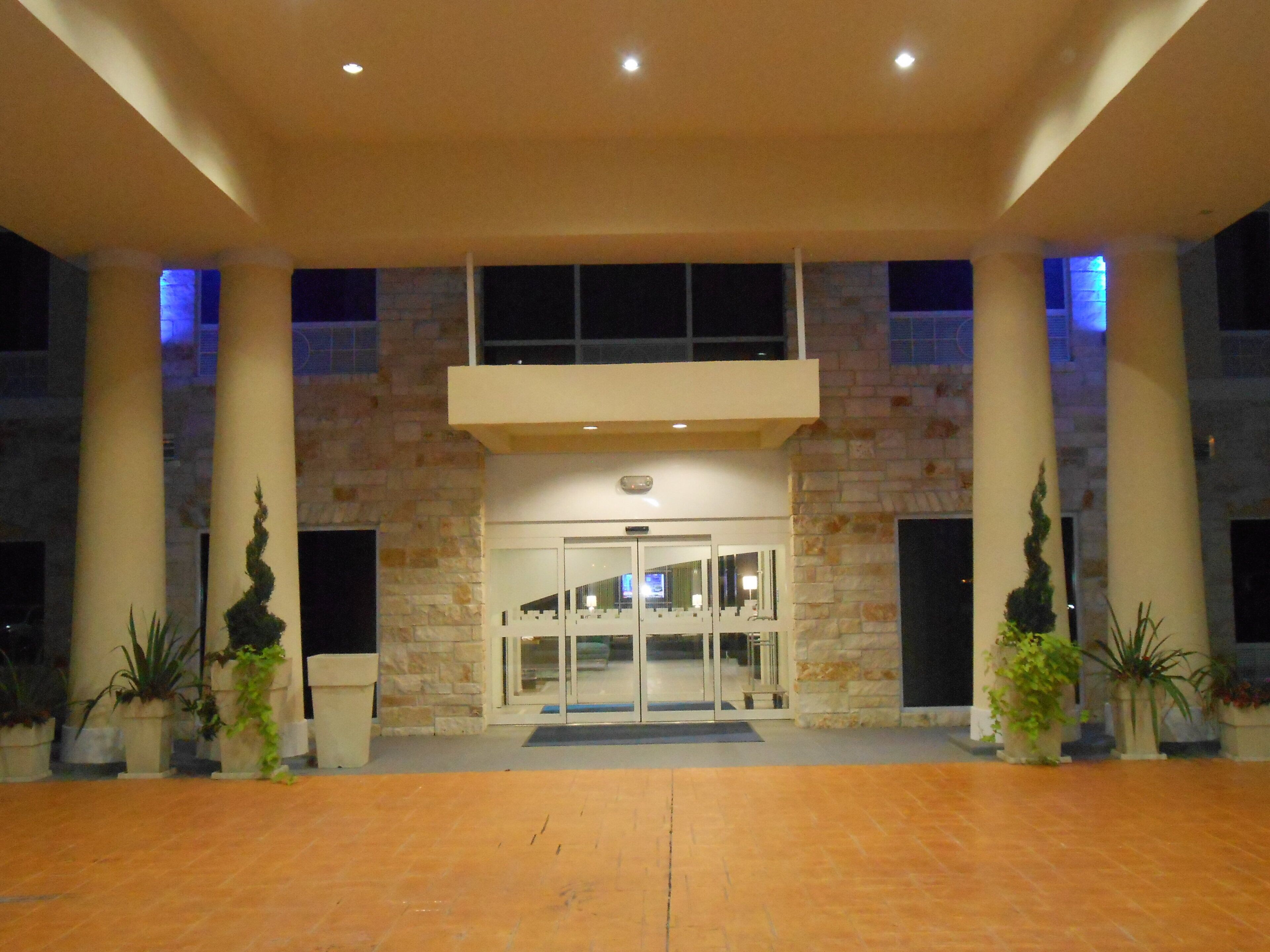 A building entrance with a glass door, stone columns, and potted plants.